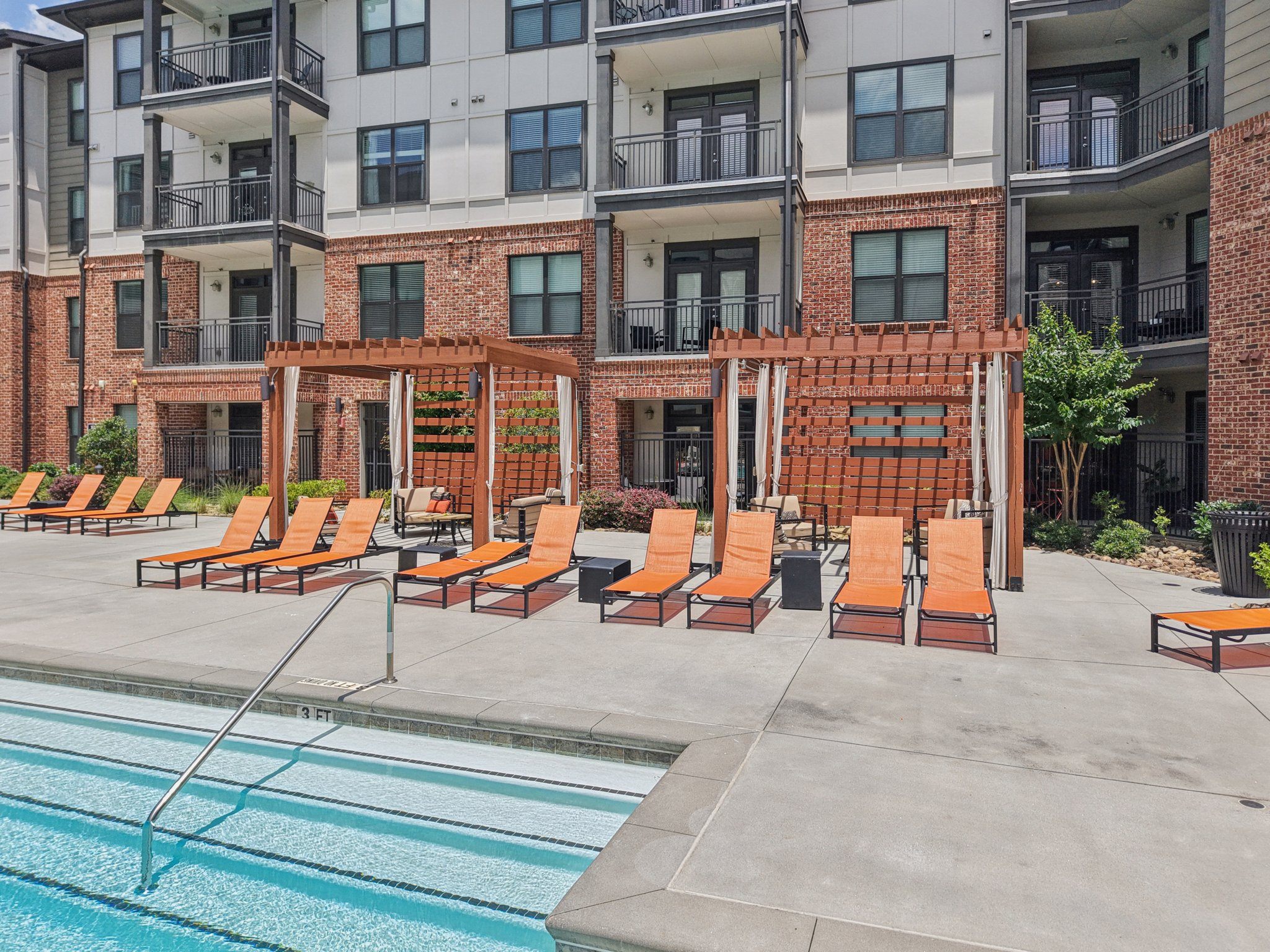 A pool area with orange chairs and a brick building in the background.